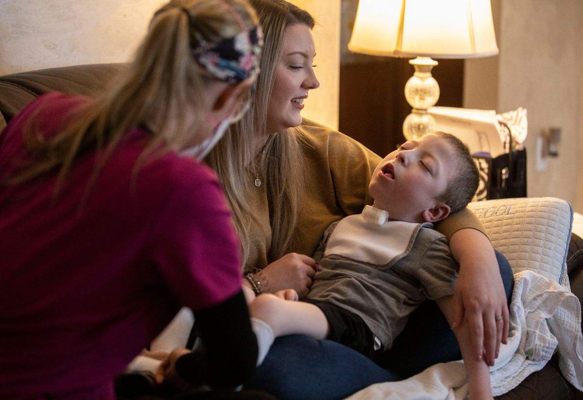 Claudia Moore holds her son Boston Yannotti, 5, who has an ultra-rare disease called AADC deficiency, while Missy Bailey, a home health nurse, puts stabilizing boots on Boston at their home in Eden, N.C. on March 9, 2022.