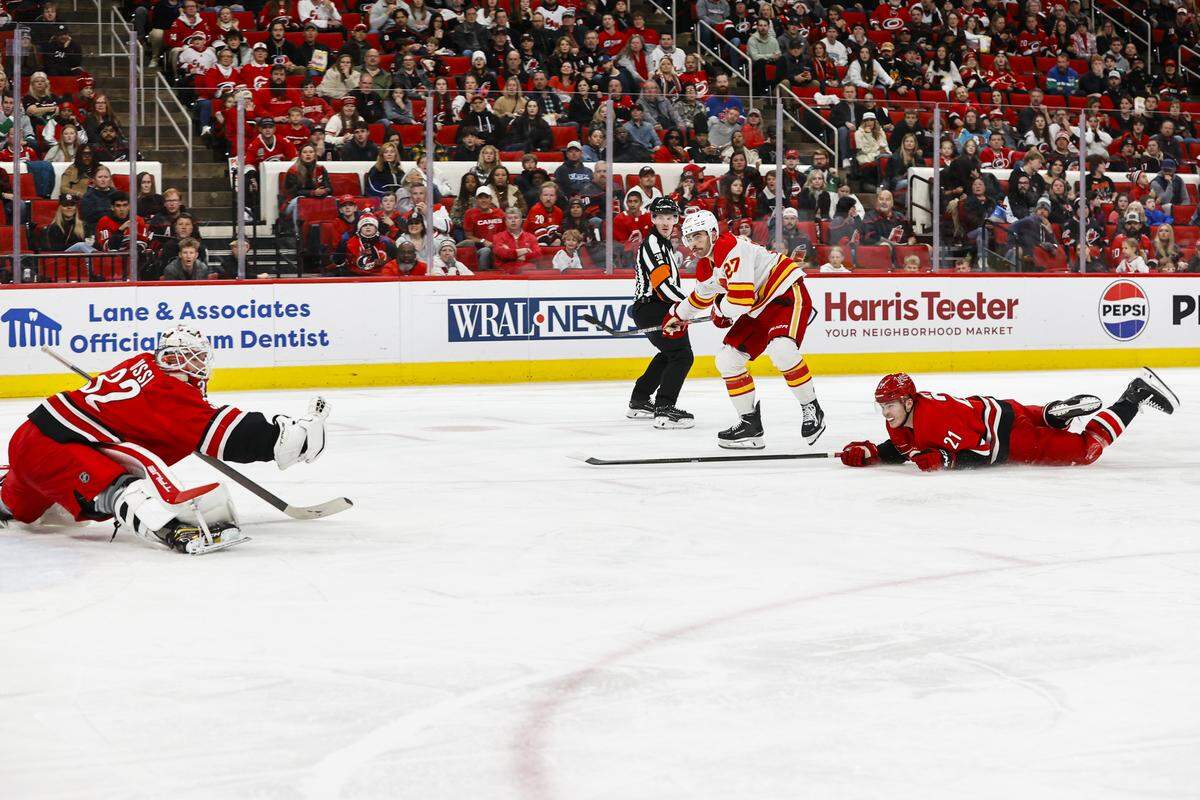 Carolina Hurricanes goalie Brandon Bussi makes a save on the Calgary Flames’ Matt Coronato (27) while Alexander Nikishin defends during the third period at Lenovo Center on Nov. 30, 2025 in Raleigh, North Carolina.