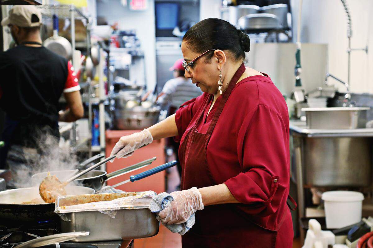 Plaza Cafe chef and owner Ravinder Kaur, center, prepares orders in the kitchen. The family-owned business in downtown Raleigh estimates that they have lost thousands of dollars in profits with conferences canceled and many customers working from home.