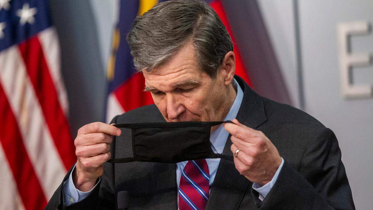Gov. Roy Cooper puts on a mask after speaking during a briefing on North Carolina’s coronavirus pandemic response Wednesday, Jan. 27, 2021 at the NC Emergency Operations Center in Raleigh.