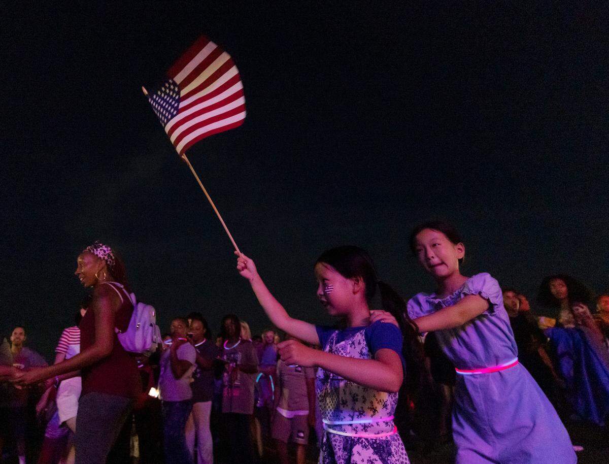 Riyoon Kwon, 8, holds an American flag aloft while dancing with her sister, Jaeyoon Kwon, 11, during an Independence Day celebration at Dorothea Dix Park on Tuesday, July 4, 2023, in Raleigh, N.C.