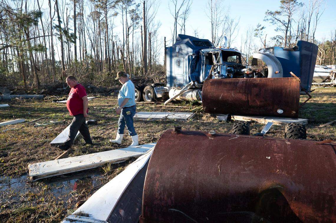 Releon Brown and Jeff Green walk among damaged tractor trailers at Greens business on Green Bay Road on Tuesday, February 16, 2021 in Brunswick County after a tornado moved through the area on Monday night.