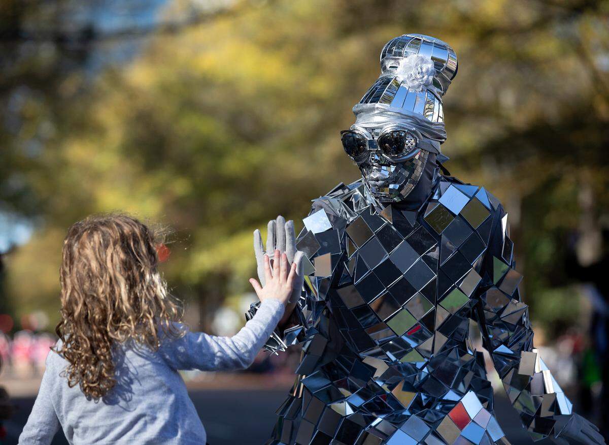 A performer from Imagine Circus high fives a young child during the Raleigh Christmas Parade on Saturday, Nov. 18, 2023.
