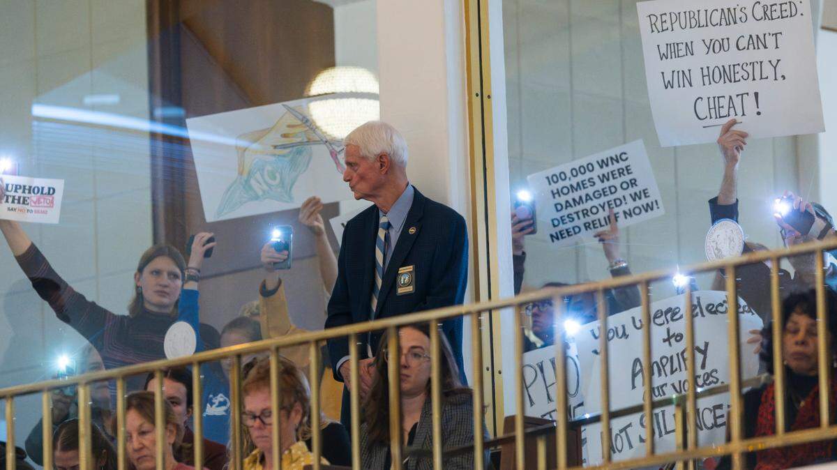 Demonstrators hold signs outside a gallery window overlooking the North Carolina House floor before the House voted to override Gov. Roy Cooper’s veto of a Helene relief bill that reduces the power of incoming Democrats in the executive branch during a session on Wednesday, Dec. 11, 2024 at the North Carolina Legislative Building. Cooper vetoed Senate Bill 382 on Nov. 26, calling it “a sham” and criticizing it for lacking hurricane relief and including various power grabs.