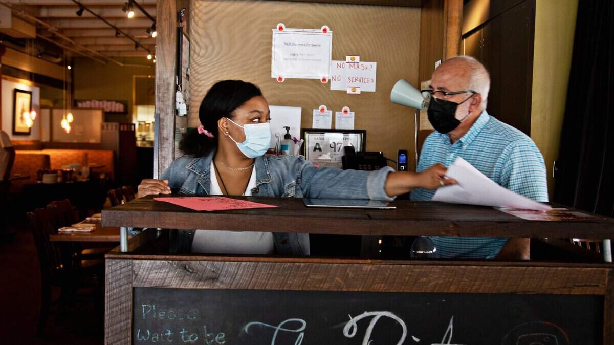 The Pit hostess Aseelah Muhammad, left, and general manager Robert Berbary, right, gather menus at the start of lunch on Aug. 16, 2021. The Pit staff are fully masked and the Raleigh restaurant has posted signs asking customers to mask up for the citywide mask mandate.