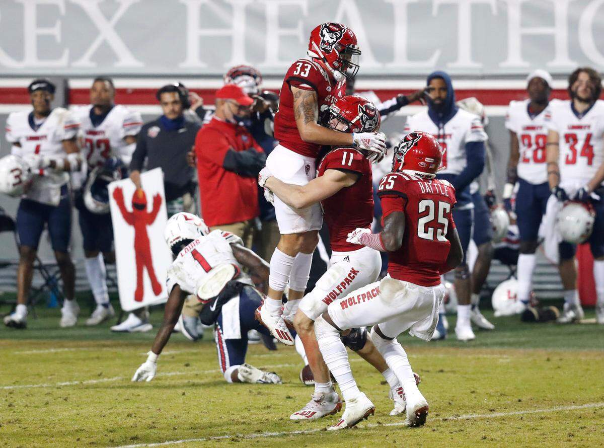N.C. State linebacker Payton Wilson (11) lifts up cornerback Isaac Duffy (33) after Duffy intercepted the pass during the second half of N.C. State’s 15-14 victory over Liberty at Carter-Finley Stadium in Raleigh, N.C., Saturday, Nov. 21, 2020. N.C. State cornerback Shyheim Battle (25) also comes in to celebrate.