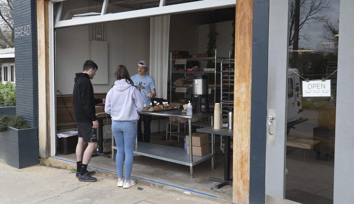 Sam Wilson fills a order for Jade and Kilian Bouedo of Cary, N.C., at Boulted Bread on South Street on Wednesday morning, March 18, 2020 in Raleigh, N.C. With restrictions on gathering inside due to the spread of the COVID-19 virus, small businesses like Boulted have to be creative to continue serving customers and keep their businesses open. Boulted moved operations to the sidewalk and are only taking credit cards.