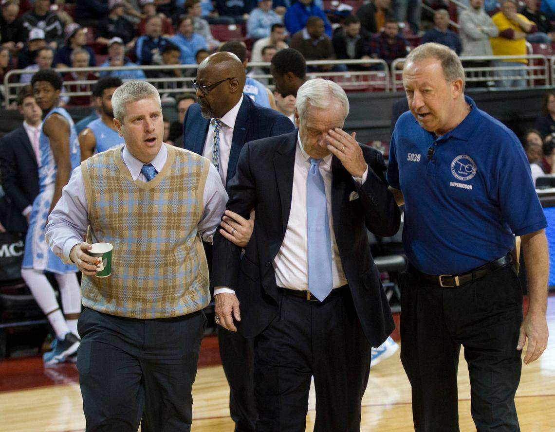 North Carolina coach Roy Williams is escorted off the court early in the second half of play against Boston College on Tuesday, January 9, 2016 at Conte Forum in Chestnut Hill, Mass. Williams appeared to faint and sat on the floor surrounded by players during the time out, and had trouble getting to his feet, before being assisted off the court. Assistant coach Steve Robinson took over in Williams’ absence. Williams appeared following the game and said he had a vertigo attack
