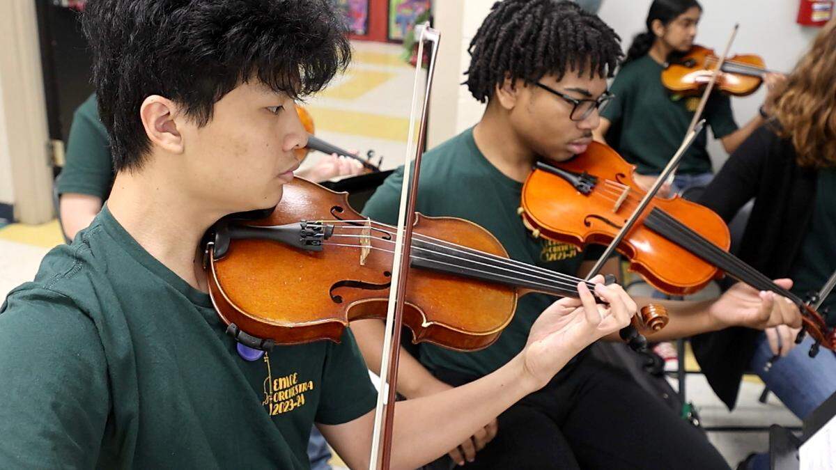 Members of the Enloe High School orchestra including Nathan Fan, left, and Tristan Meyers play during the Silver Tray Luncheon at Combs Elementary School in Raleigh, N.C., Thursday, May 16, 2024. At the Silver Tray Luncheon, cafeteria tables have table clothes, centerpieces and ‘fancy’ silverware as the Enloe High School orchestra plays music to provide a fine dining experience. It’s a way for students to practice the social etiquette skills they’re learning. 