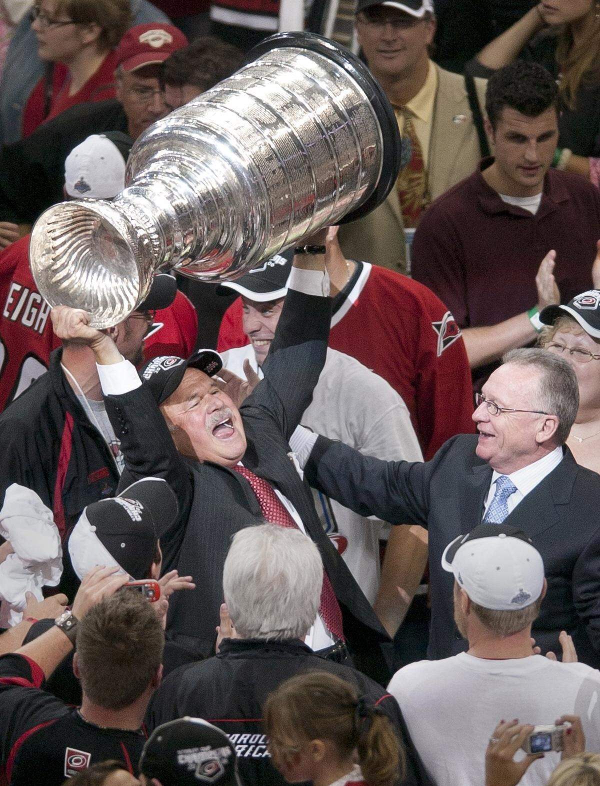 The Carolina Hurricanes team owner Peter Karmanos Jr. , left, hoists the Stanley Cup after his team defeated the Edmonton Oilers 3-1 in Game Seven of the Stanley Cup Finals played in Raleigh on June 19, 2006 as the Canes general manger Jim Rutherford looks on at right.