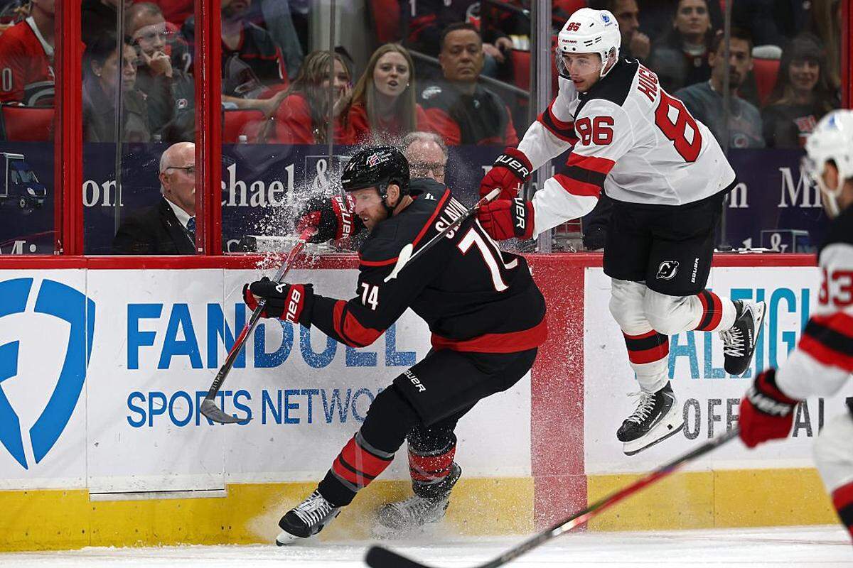 Jack Hughes of the New Jersey Devils avoids a check from Jaccob Slavin of the Carolina Hurricanes during the first period of the game at Lenovo Center on October 09, 2025 in Raleigh, North Carolina.