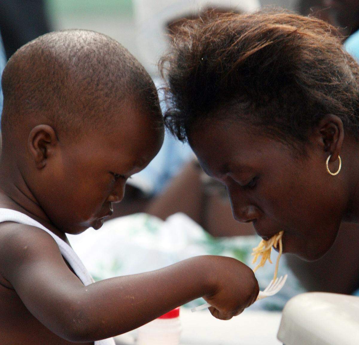 A young boy feeds his mother outside the hospital building he had been in. His leg had been amputated in Port Au Prince.