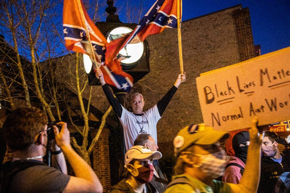 Thomas May holds two Confederate flags while standing above a crowd of anti-racist protesters as they enter Court Square in downtown Graham for an Election Day rally on Nov. 3, 2020.