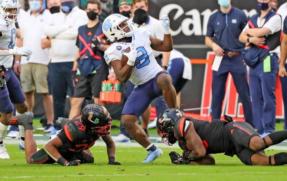 Miami Hurricanes linebacker Zach McCloud (53) and cornerback Isaiah Dunson (29) stop North Carolina Tar Heels running back Michael Carter (8) in the second quarter at Hard Rock Stadium In Miami Gardens, Florida, Saturday, December 12, 2020.