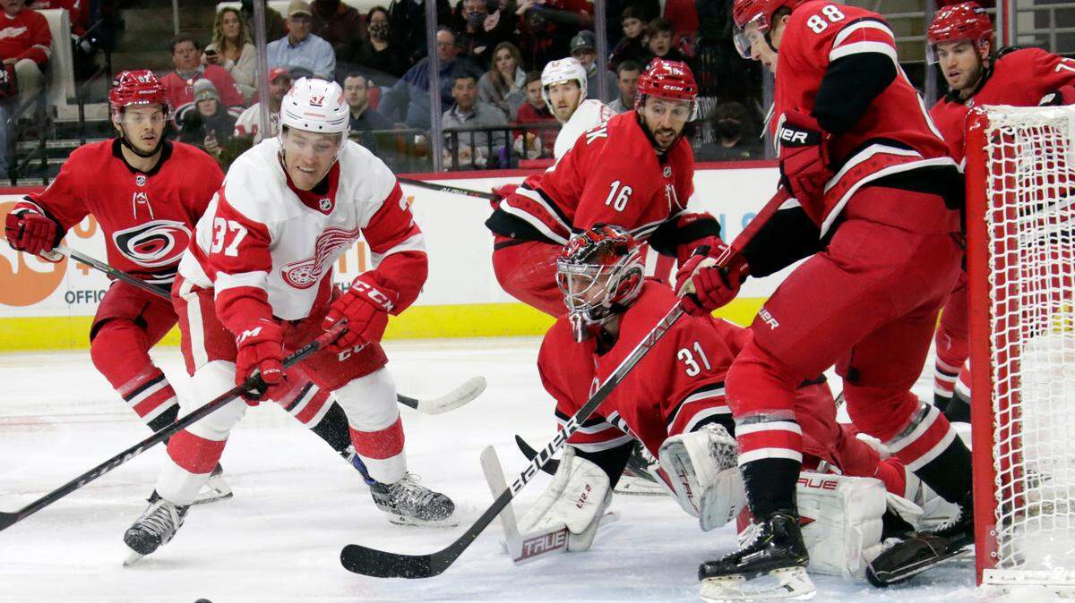 Detroit Red Wings center Carter Rowney (37) is defended by Carolina Hurricanes goaltender Frederik Andersen (31), center Vincent Trocheck (16) and center Martin Necas (88) as he works near the net during the first period of an NHL hockey game Thursday, Dec. 16, 2021, in Raleigh, N.C. (AP Photo/Chris Seward)