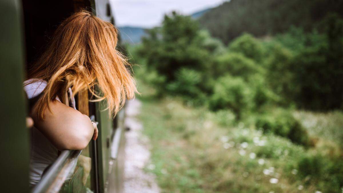 A woman looking out the window of a train at the green landscape. 