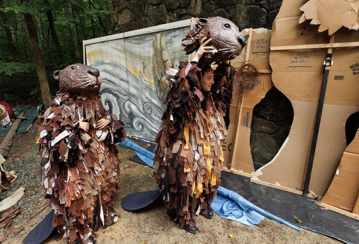 Sophia Joy, right, a puppeteer with Paperhand Puppet Intervention, puts on a beaver mask while preparing to take the stage during a rehearsal for the company’s production,“The Gift,” on Tuesday, Aug. 12, 2025, at the Forest Theatre in Chapel Hill, N.C.