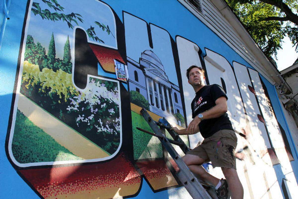 Scott Nurkin, 37, is modeling his mural on the back wall of He’s Not Here on a classic Greetings from Chapel Hill postcard by German printer Curt Teich.