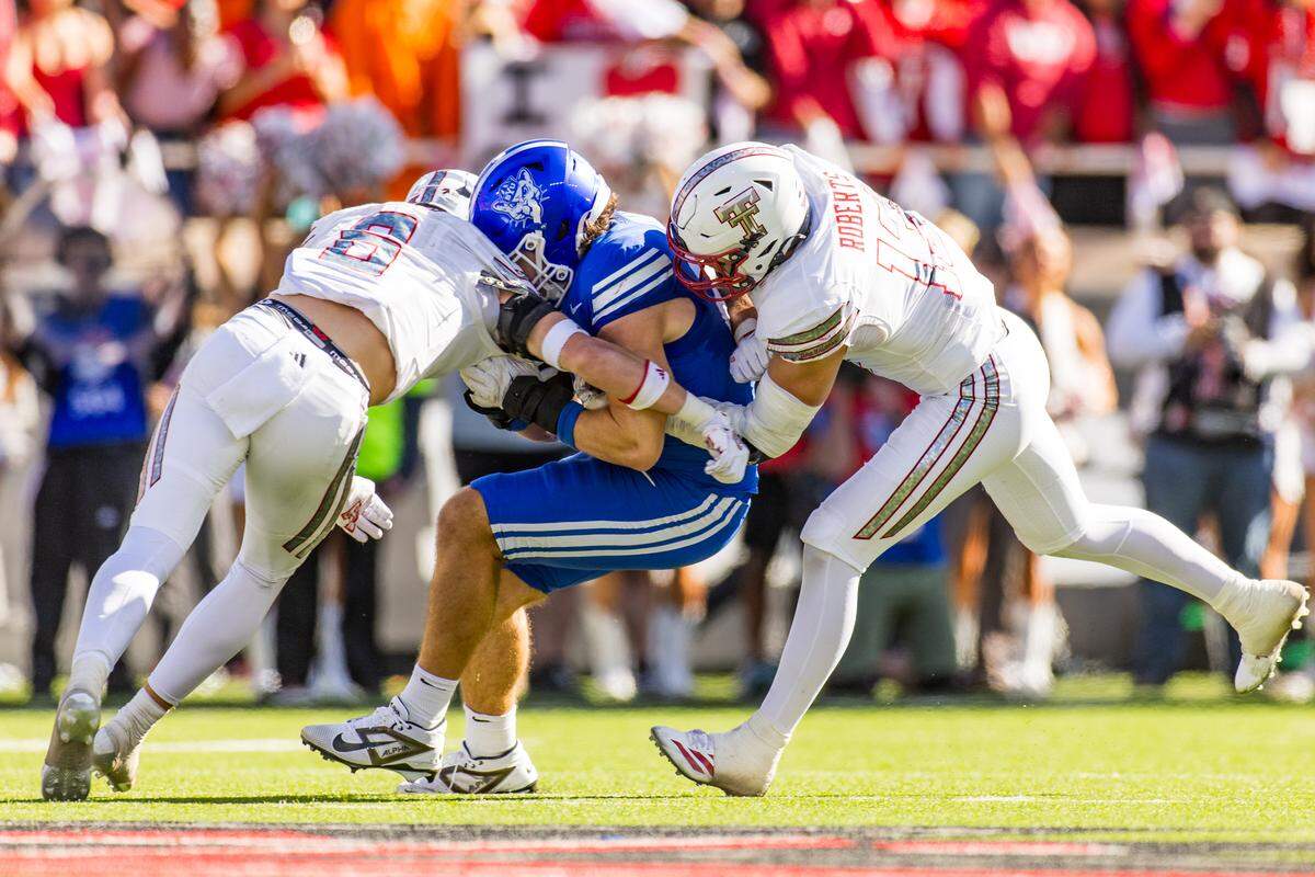 John Curry, left, and Ben Roberts of the Texas Tech Red Raiders tackle Carsen Ryan of the BYU Cougars during the second half of the game at Jones AT&T Stadium on Nov. 8, 2025 in Lubbock, Texas. 