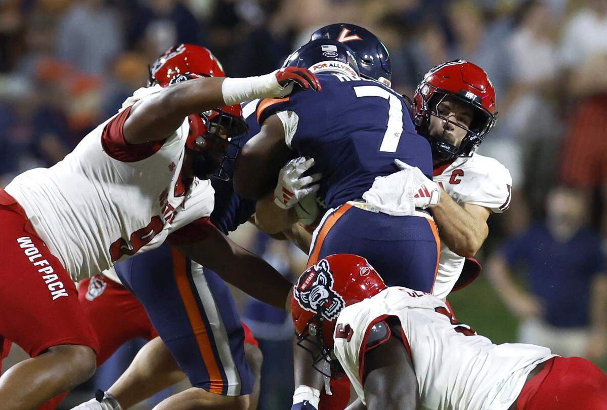N.C. State’s Payton Wilson (11) and Savion Jackson (9) stop Virginia running back Mike Hollins (7) during the first half of N.C. State’s game against Virginia at Scott Stadium in Charlottesville, Va., Friday, Sept. 22, 2023.