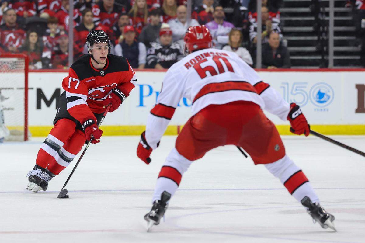 Apr 25, 2025; Newark, New Jersey, USA; New Jersey Devils defenseman Simon Nemec (17) skates with the puck as Carolina Hurricanes left wing Eric Robinson (50) defends during the first overtime in game three of the first round of the 2025 Stanley Cup Playoffs at Prudential Center. Mandatory Credit: Ed Mulholland-Imagn Images