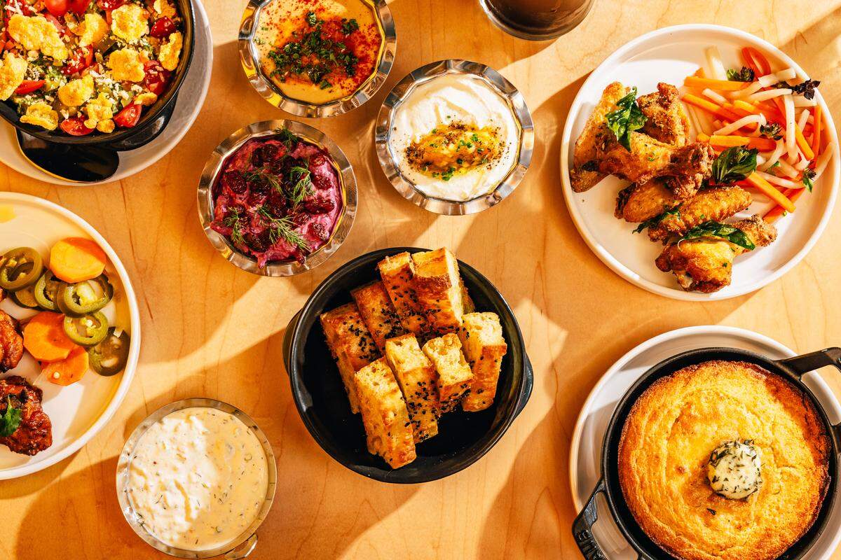A collection of dishes from the new restaurant Big Cat in Raleigh, including nine layer dip, mezze with whipped feta and tzatziki, chicken wings and cornbread with curry leaf butter.