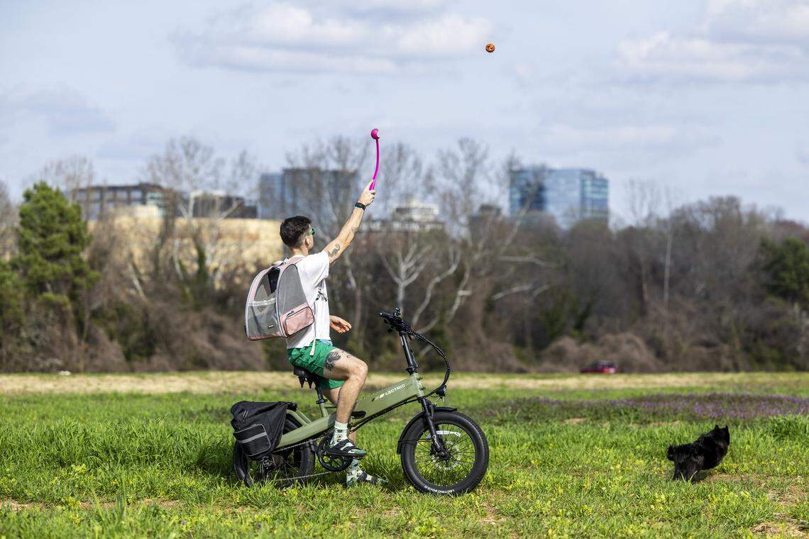 Andrew Gregg plays fetch with his 6-year-old rescue dog, Bubs, while riding his e-bike at Dorothea Dix Park with the Raleigh skyline in the background on Thursday, March 5, 2026, as temperatures climbed into the upper 70s during one of the final days of winter. Clocks spring forward at 2 a.m. Sunday, March 8, shifting sunset later into the evening and signaling longer days ahead. Gregg says Bubs often rides in a pet carrier backpack with him on outdoor adventures when the weather is nice.