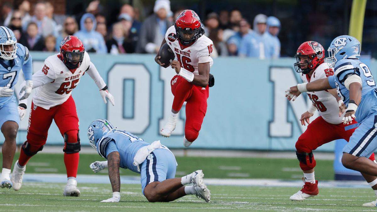 N.C. State quarterback CJ Bailey (16) jumps over North Carolina linebacker Amare Campbell (17) during the first half of N.C. State’s game against UNC at Kenan Stadium in Chapel Hill, N.C., Saturday, Nov. 30, 2024.