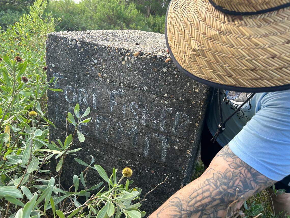 Rob Hill pulls back brush from the gateway near the World War II bunker where Robert Harrill, the Fort Fisher Hermit, lived south of Wilmington, which includes an inscription in his own hand.