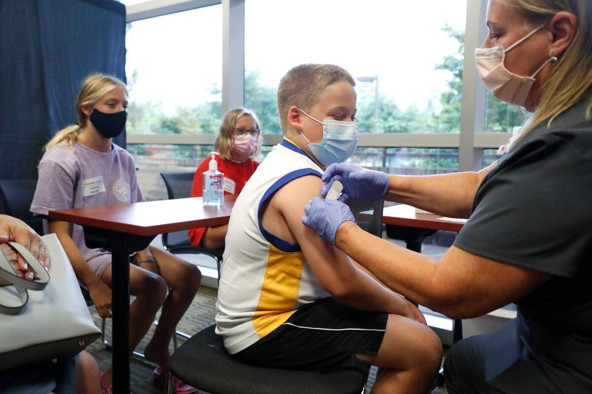 Eli Strickland, 12, gets a band aid after getting his first COVID-19 vaccine shot from Pam Scott, RN, during the WakeMed Back-to-School Blitz vaccine clinic at the WakeMed Raleigh Campus in Raleigh, N.C., Sunday, August 1, 2021. Eli’s sisters, they are triplets, Campbell, left, and Emma, watch.