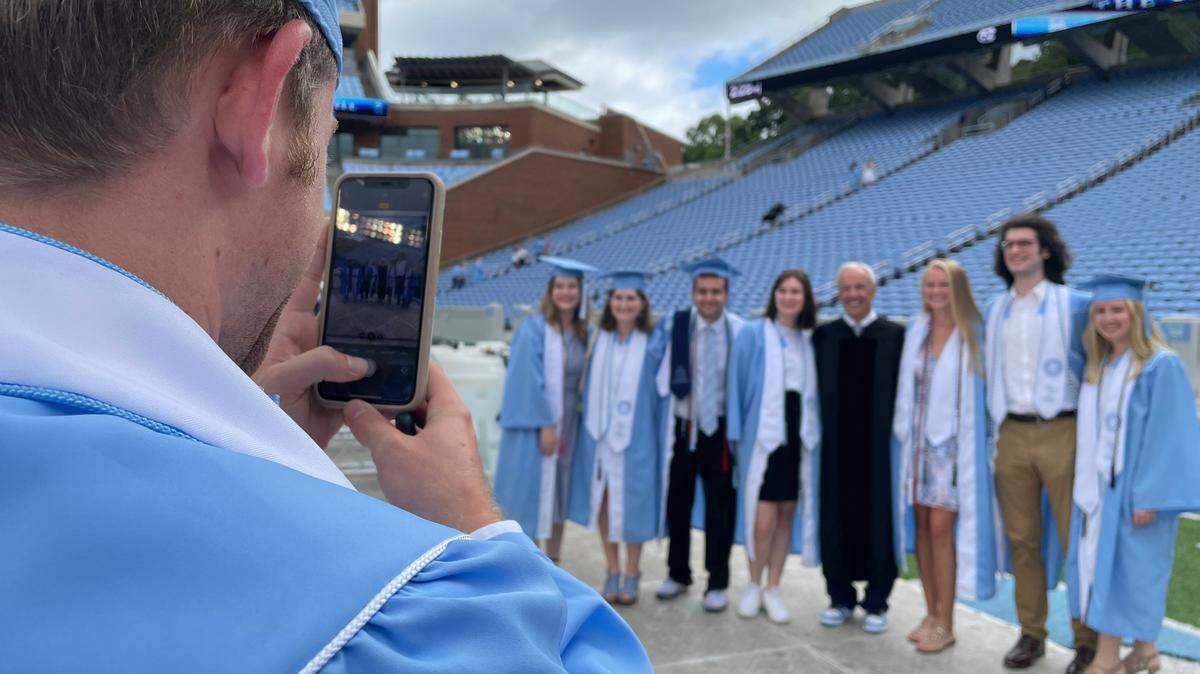A UNC-Chapel Hill 2020 graduate photographs fellow alumni posing for a photo with former UNC head basketball coach Roy Williams.