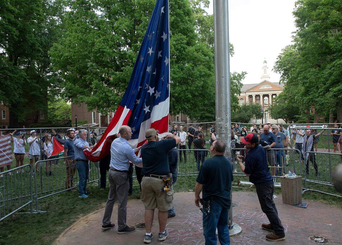 People watch as UNC-Chapel Hill administrators and facilities services staff raise an American flag behind a fenced enclosure on the campus quad on Tuesday, April 30, 2024. UNC-Chapel Hill police charged 36 members of a pro-Palestinian “Gaza solidarity encampment” Tuesday morning after warning the group to remove its tents from campus or face possible arrest, suspension or expulsion from the university. Earlier in the afternoon, protesters took an American flag down from the flagpole and then mounted a Palestinian flag in its place.