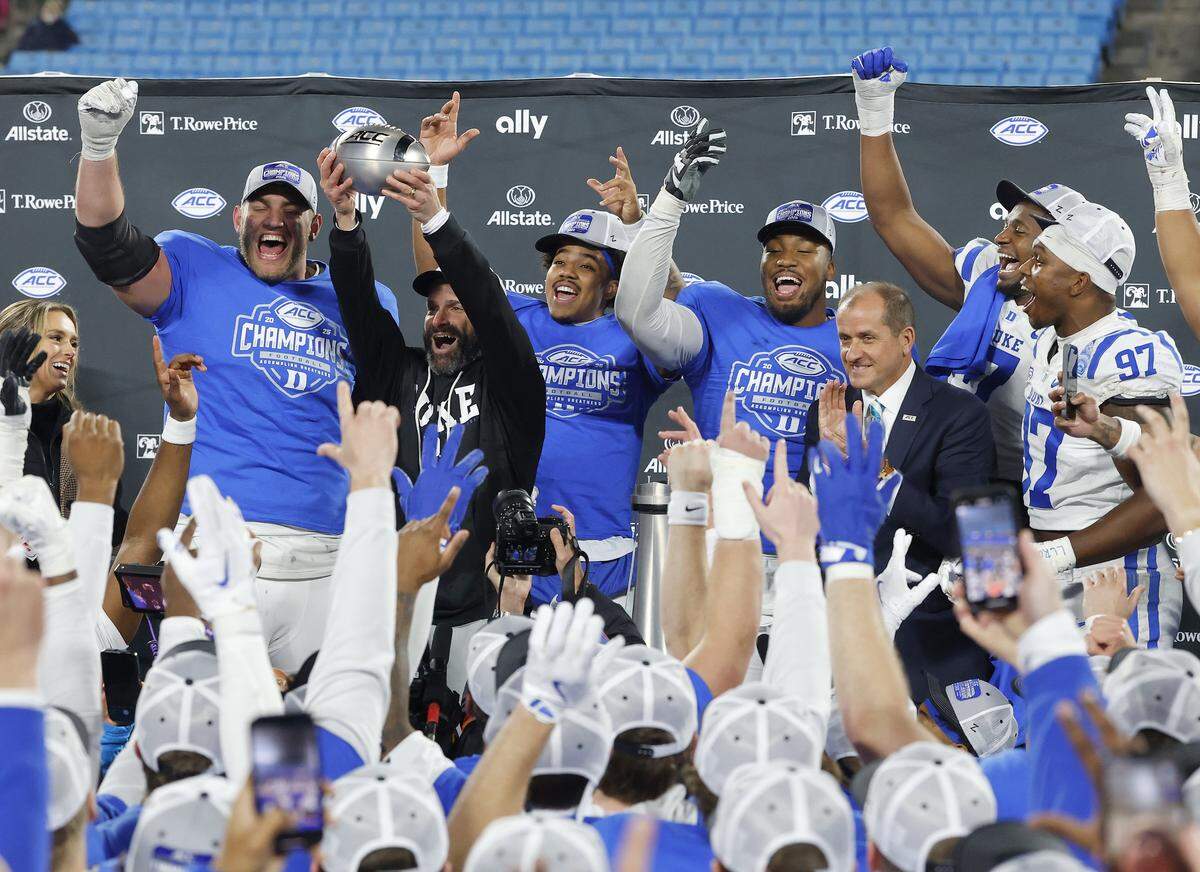 Duke head coach Manny Diaz celebrates with his team after being presented the ACC Football Championship trophy following the Blue Devils’ 27-20 overtime win over Virginia on Saturday, Dec. 6, 2025, at Bank of America Stadium in Charlotte, N.C. ACC Commissioner Jim Phillips stands to the right.