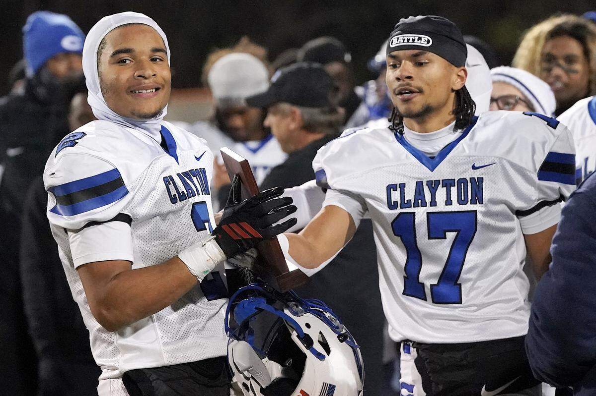 Clayton quarterback Aiden Smalls (2) and wide receiver Parker Ferguson (17) celebrate with the East Regional Champion Trophy after defeating Cardinal Gibbons. The Clayton Comets and the Cardinal Gibbons Crusaders met in the East Regional Final of the NCHSAA 7A Football Championship in Clayton, N.C. on December 4, 2025.