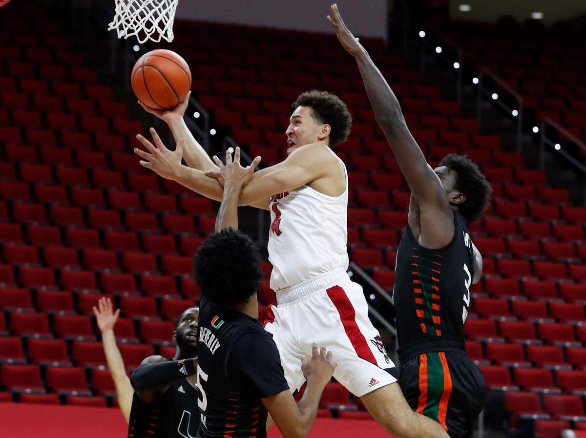 N.C. State’s Jericole Hellems (4) drives to the basket past Miami’s Harlond Beverly (5) and Nysier Brooks (3), right, during the first half of N.C. State’s game against Miami at PNC Arena in Raleigh, N.C., Saturday, January 9, 2021.