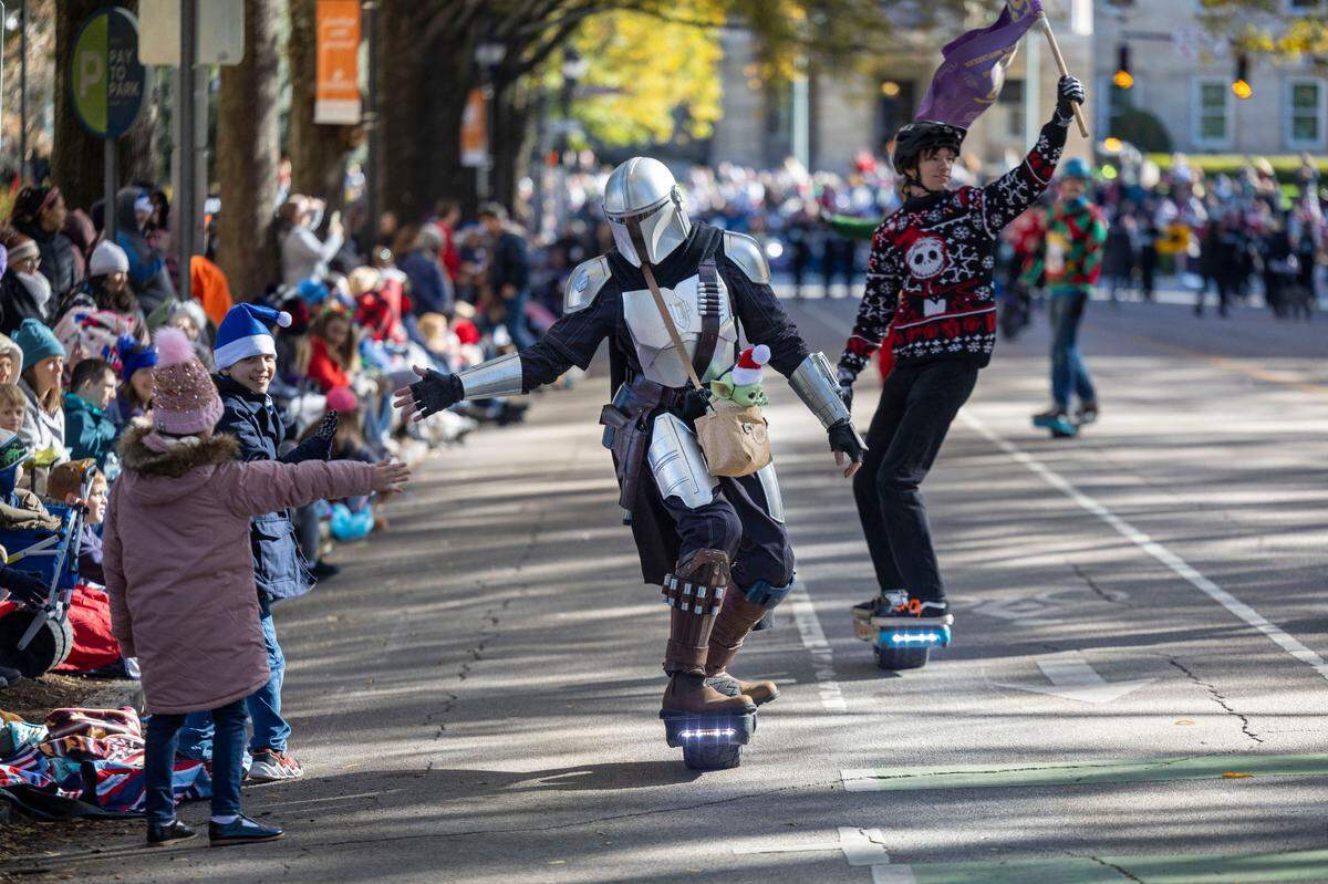 A member of the Oak City One Wheel group, dressed the Mandalorian, greets parade watchers along Hillsborough Street during the 80th annual Raleigh Christmas Parade on Saturday, November 23, 2024 in Raleigh, N.C.