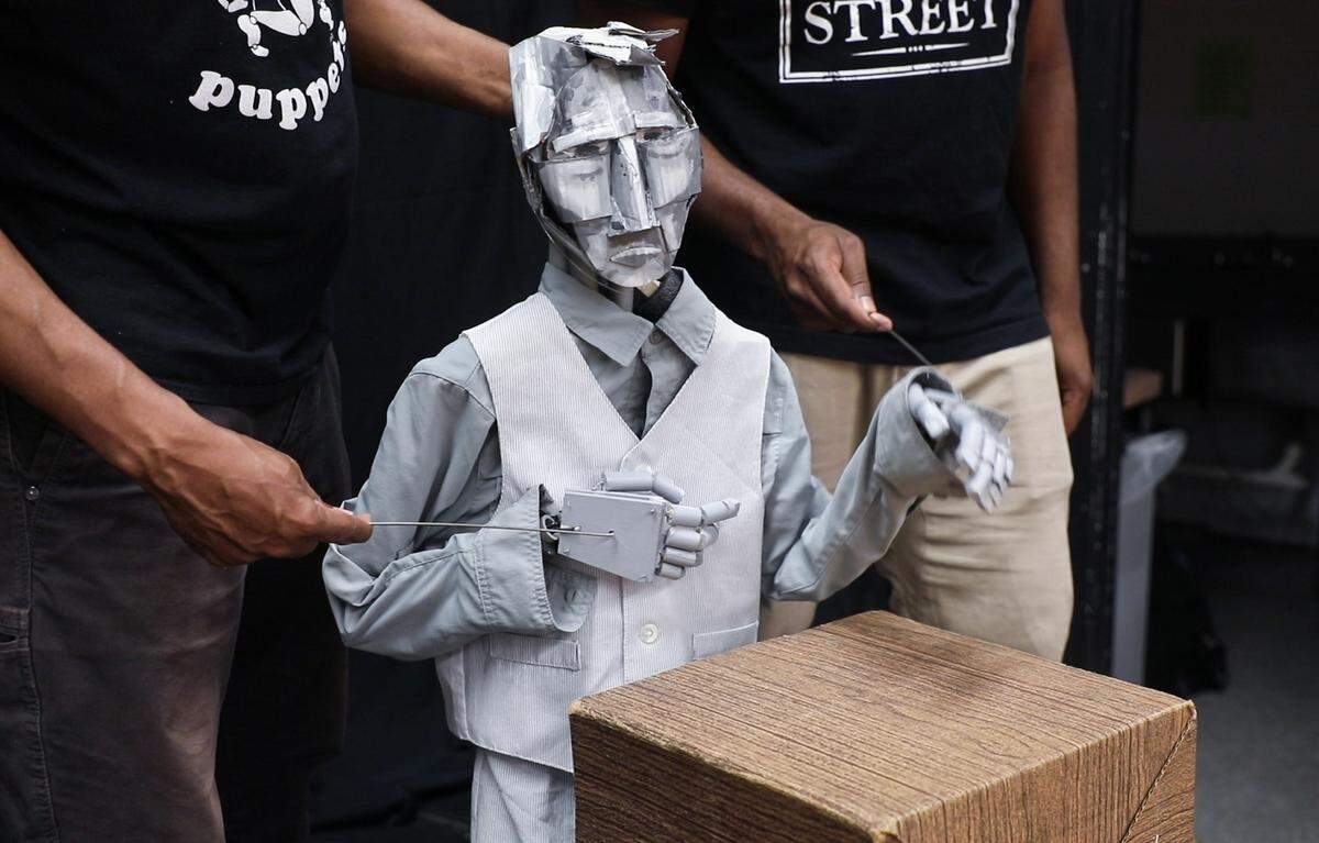 Jesse Miller, being animated by Jeghetto, left, and puppeteer Brentton Harrison, right, speaks at a podium during a rehearsal of Jeghetto's "Just Another Lynching," at The Arts Center in Carrboro on Thursday, May 31, 2018. Miller, who is white, is Cornelius Jones' childhood friend.