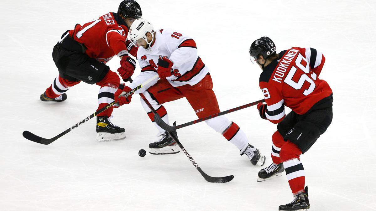 Carolina Hurricanes center Vincent Trocheck (16) plays the puck against New Jersey Devils defenseman Jonas Siegenthaler (71) and center Janne Kuokkanen (59) during the third period of an NHL hockey game, Saturday, Jan. 22, 2022, in Newark, N.J. (AP Photo/Noah K. Murray)
