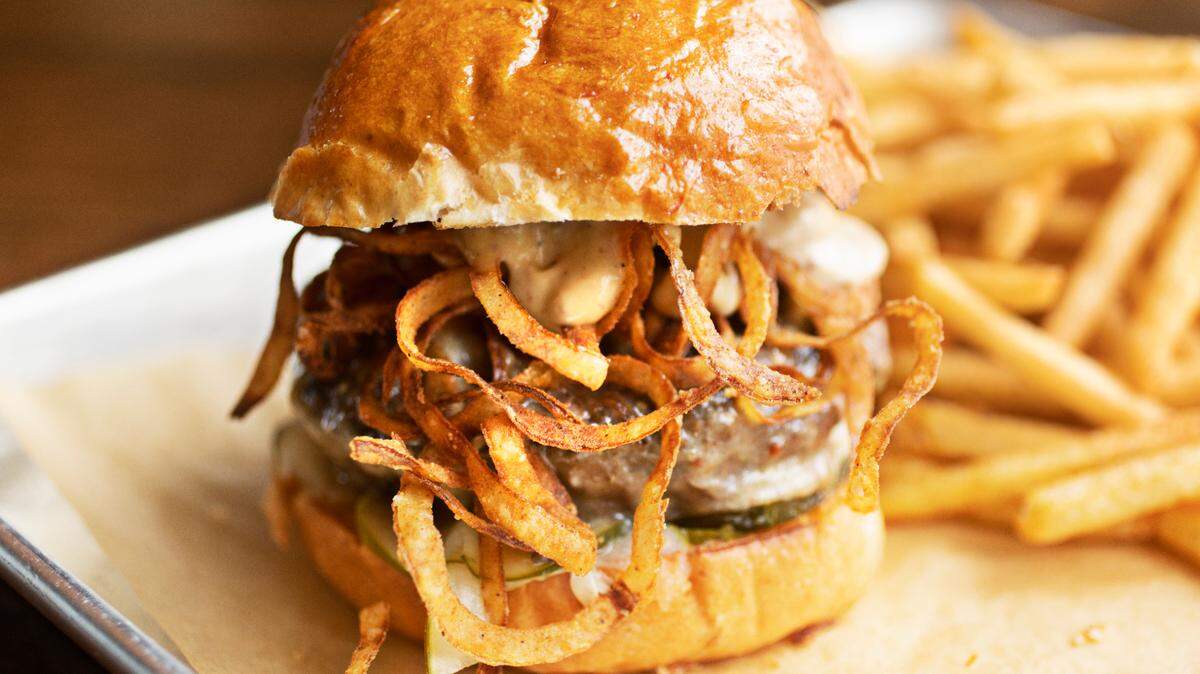 The burger at Neuse River Brewing in Raleigh is a “half-pound beef patty with beer cheese, roasted garlic mustard aioli, house-made pickles, crispy onion strings served on a Union Special Bread brioche bun with a side of fries.