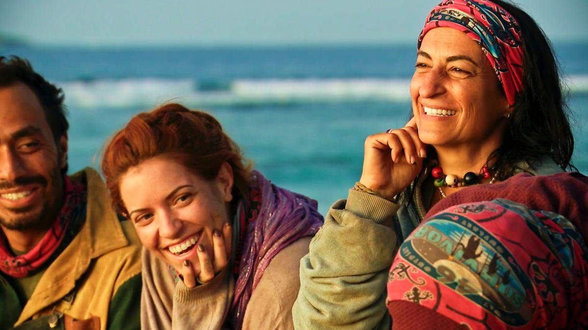 Ben Katzman, Kenzie Petty and Maria Gonzalez pictured with a body of water in the background. Katzman wears a tan jacket and red bandanna around his neck, Petty wears dark nail polish, a tan sweater and a purple scarf, and Gonzalez wears a chunky beaded necklace and multicolored chunky headband. 