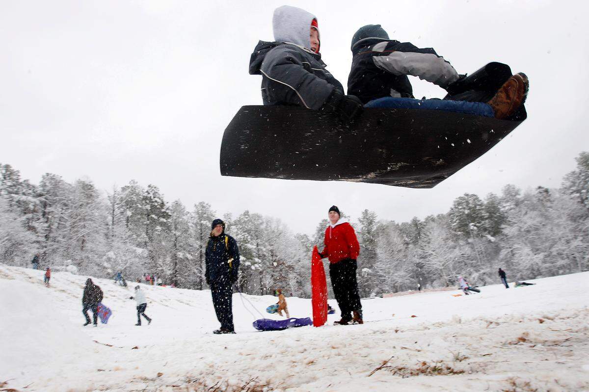 Sledders go airborne after piloting their mat over a ramp made of packed snow at Bond Park in Cary in 2010.