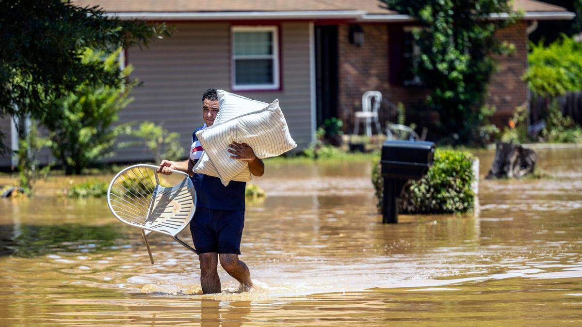 Naser Daher, of Durham’s Old Farm neighborhood, carries his belongings through floodwaters near the Eno River in Durham on Monday morning, July 7, 2025, after heavy rain from Tropical Storm Chantal caused flash flooding. Daher and his brother said they escaped the home with four children in the middle of the night as floodwater poured in.