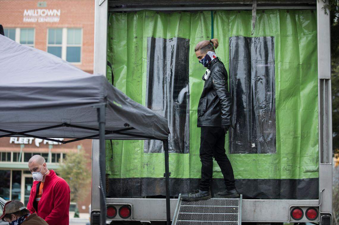 David Suarez, right, waits at the entrance to a food storage truck for another pick-up order to be called by Tally Lassiter, left, and Bill Tarman, far left, in East Main Square in Carrboro, N.C. on Tuesday, March 31, 2020. The Carrboro United Local Food Hub coordinates distribution of family style meals and goods from local restaurants in an effort to safely feed people while reinvigorating the local economy for the duration of the COVID-19 outbreak.