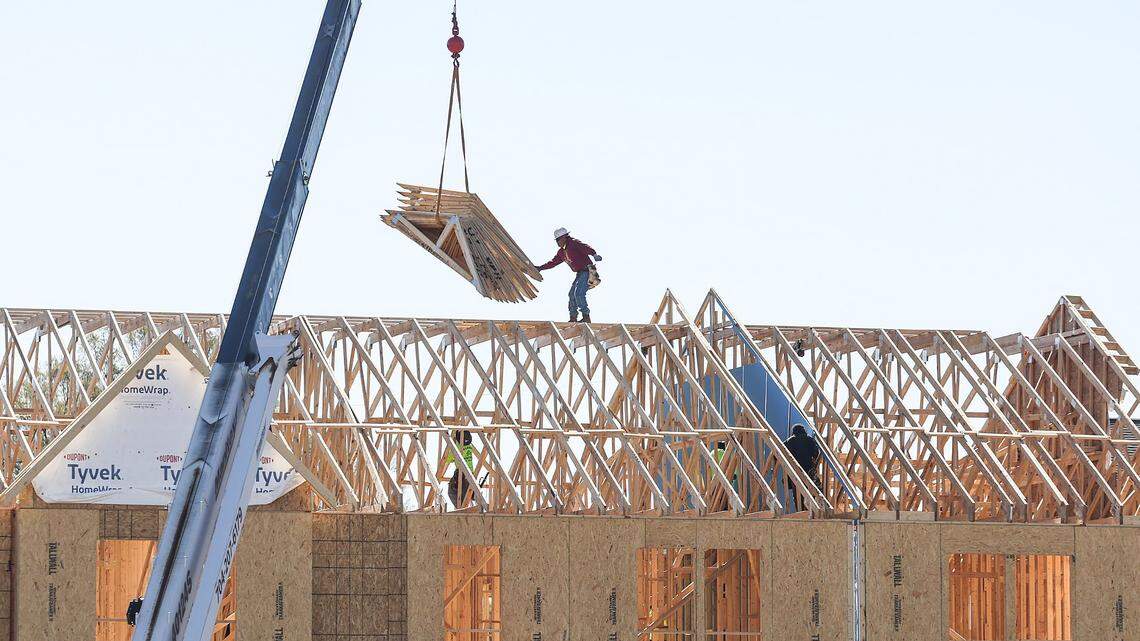 Perched atop the roof of townhomes under construction near Charlotte’s University City neighborhood, a worker reaches for a load of trusses from a crane.