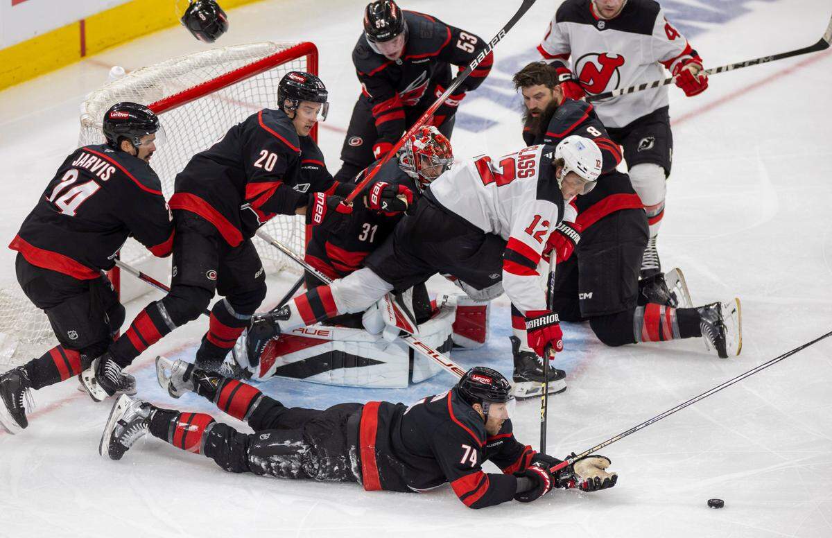 Carolina Hurricanes defenseman Jaccob Slavin (74) covers the puck, teammate Brent Burns (8) looses his helmet as they assist Hurricanes goalie Frederik Andersen (31) on a scoring attempt by the New Jersey Devils center Cody Glass (12) in the second period during game two of their Stanley Cup playoff series on Tuesday, April 22, 2025 at Lenovo Center in Raleigh, N.C.
