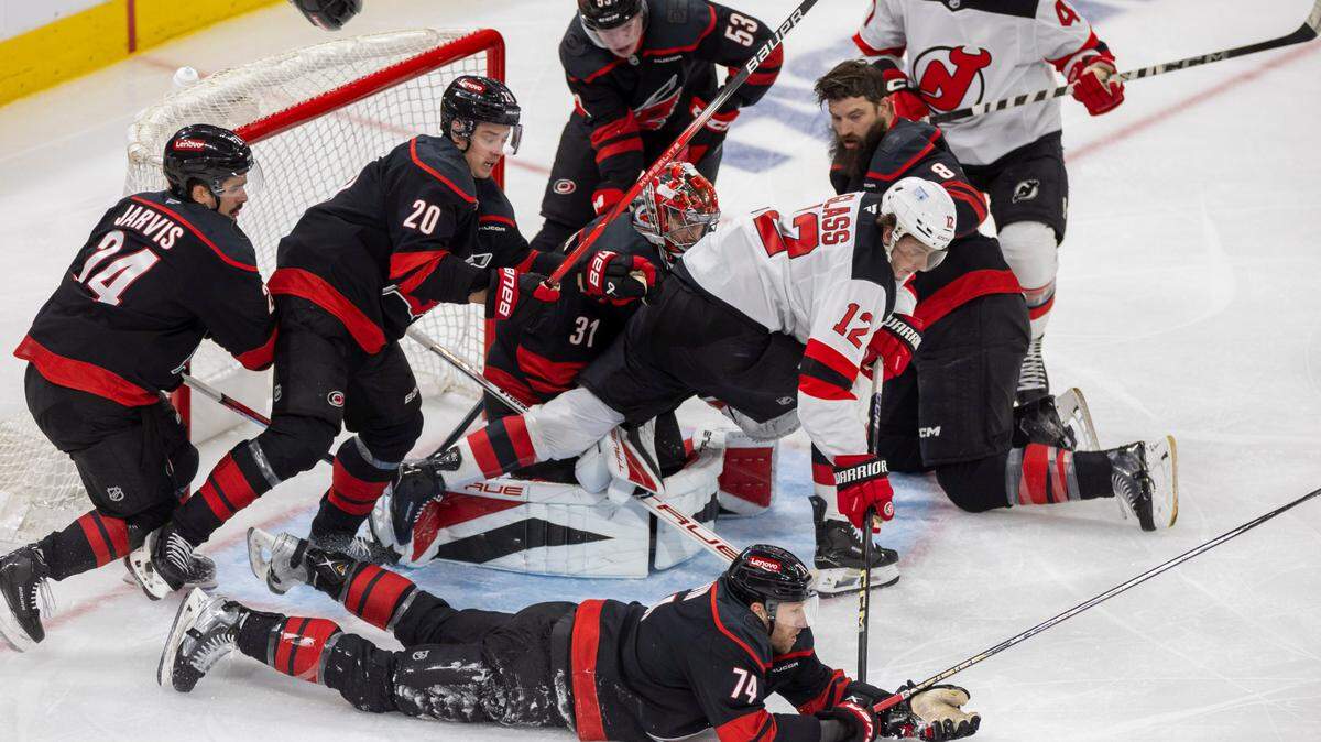 Carolina Hurricanes defenseman Jaccob Slavin (74) covers the puck, teammate Brent Burns (8) loses his helmet as they assist Hurricanes goalie Frederik Andersen (31) on a scoring attempt by the New Jersey Devils center Cody Glass (12) in the second period during game two of their Stanley Cup playoff series on Tuesday, April 22, 2025 at Lenovo Center in Raleigh, N.C.