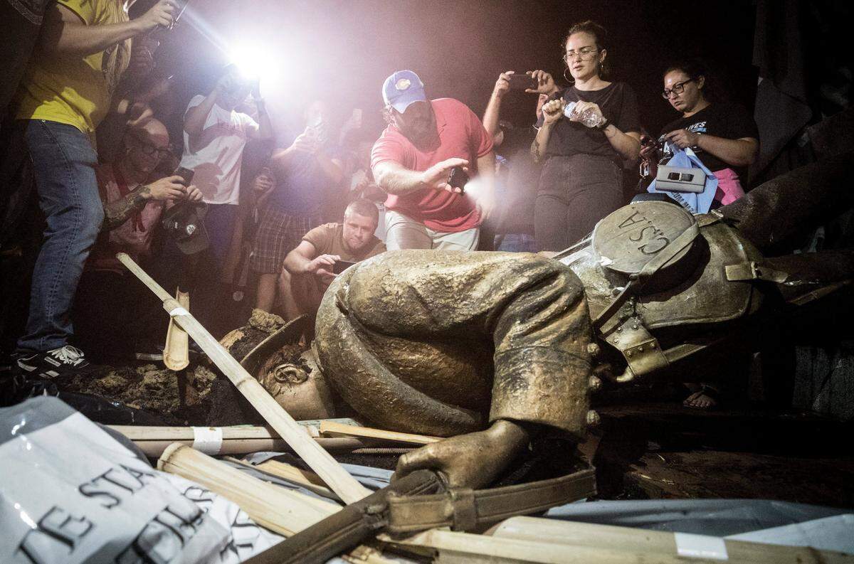 Demonstrators and spectators gather around a toppled Confederate statue known as Silent Sam Monday, August 20, 2018 at UNC-Chapel Hill. Demonstrators surrounded and obscured the statue with large banners before toppling it.