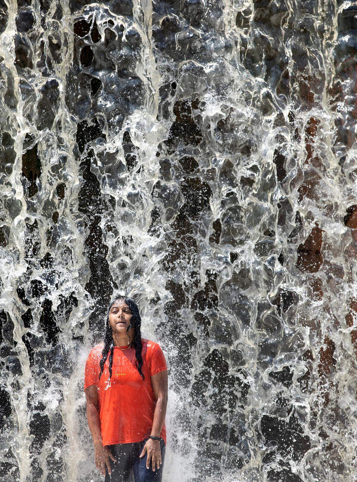 A person stands beneath cascading water at RiverPark at Cooleemee Falls on Saturday, Aug. 5, 2023, in Woodleaf, N.C.