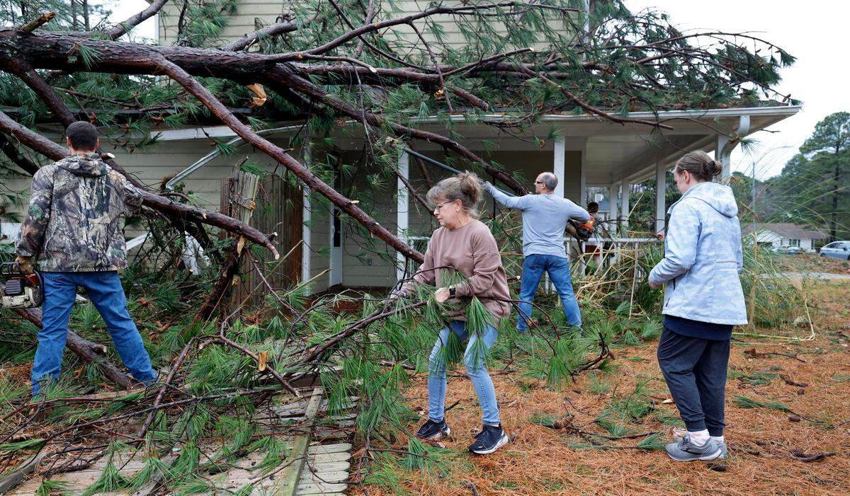 Lisa Stanley, center, and friends start to clean up knocked down trees that hit her son, Griffin’s, home on Buckhorn Road in Garner, N.C., Sunday, Dec. 10, 2023. Lisa said after the storm passed she texted her circle group from Holland’s Church and people showed up to help out. “What an awesome church family” said Stanley.