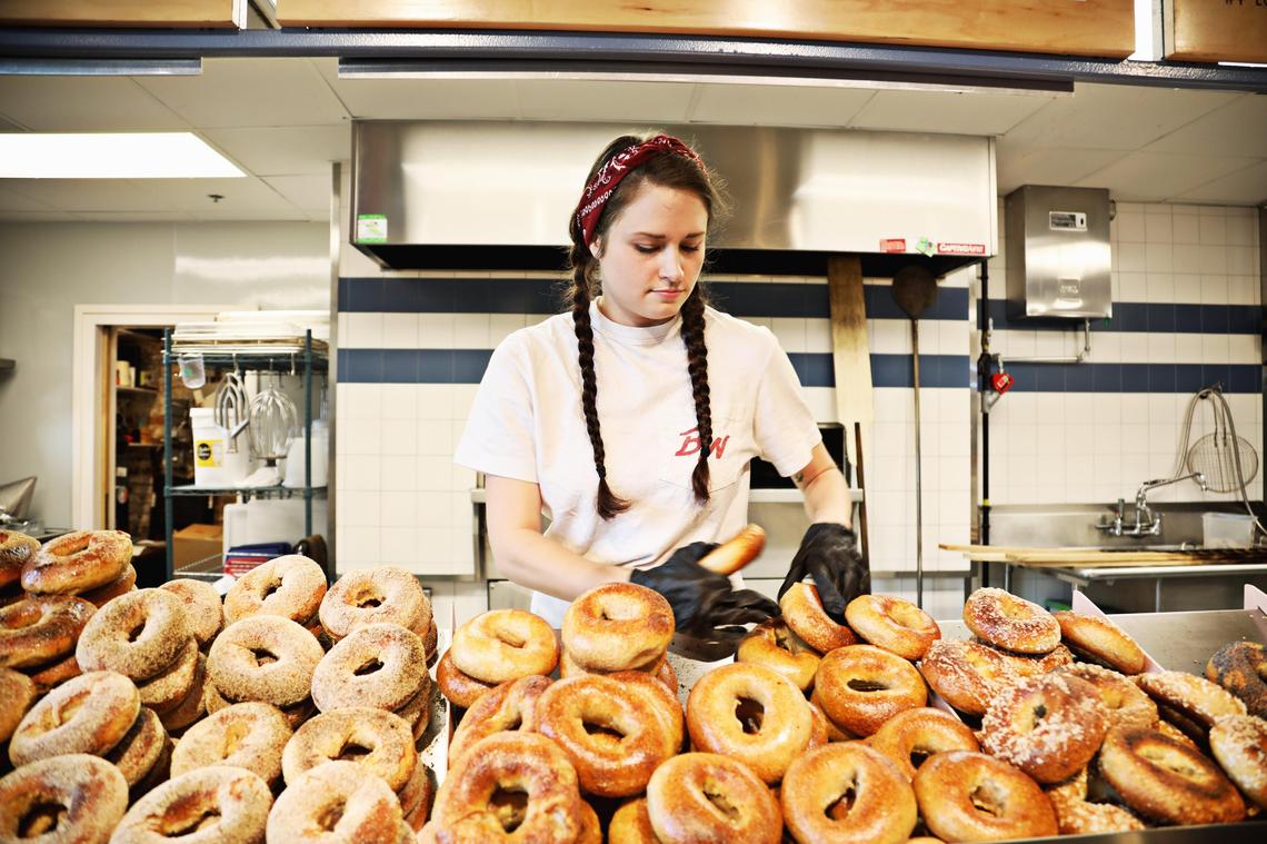 Baker Ava Broadwell adds freshly baked bagels from the wood-fired oven into the bagel bins on Tuesday morning, Oct.15, 2019, at Benchwarmers Bagels in Transfer Co. Food Hall.